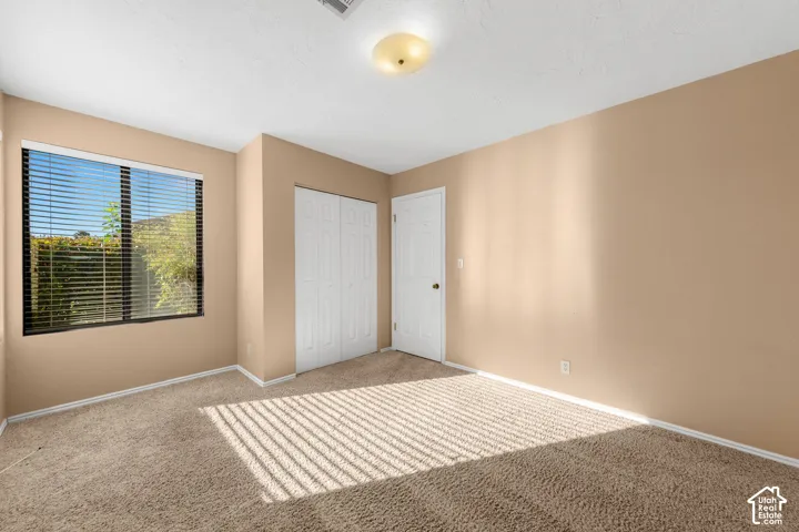 Bedroom 2. Neutral-toned wall paint with a window featuring horizontal blinds, textured carpet flooring, and a flush mount ceiling light