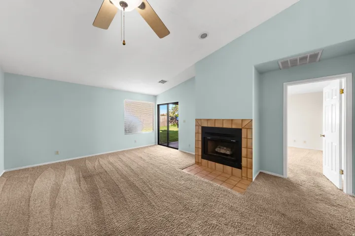 Carpeted living space featuring a tiled fireplace with hearth, ceiling fan, and sliding glass door