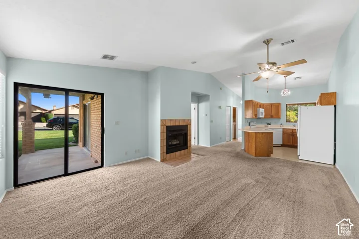 Open-concept living space featuring a fireplace with a brick surround, sliding glass door to an outdoor patio, and a kitchen with wood cabinetry.