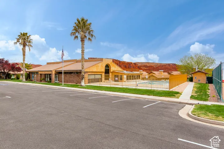Expansive parking area, stucco exterior, multiple palm trees, fenced outdoor pool, and tennis court