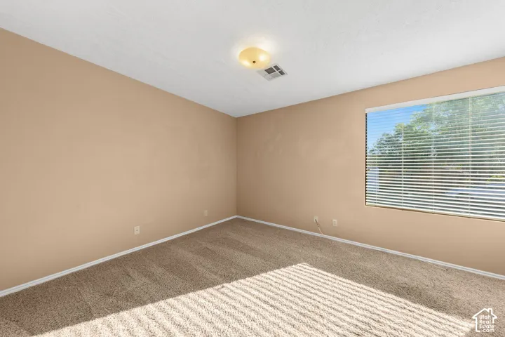 Bedroom 2. Carpeted room with neutral-toned walls, a large window with horizontal blinds, and a flush-mount ceiling light fixture