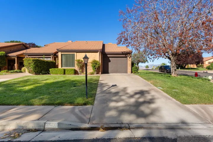Brick exterior with a tiled roof, mature landscaping, and an attached garage with a paved driveway