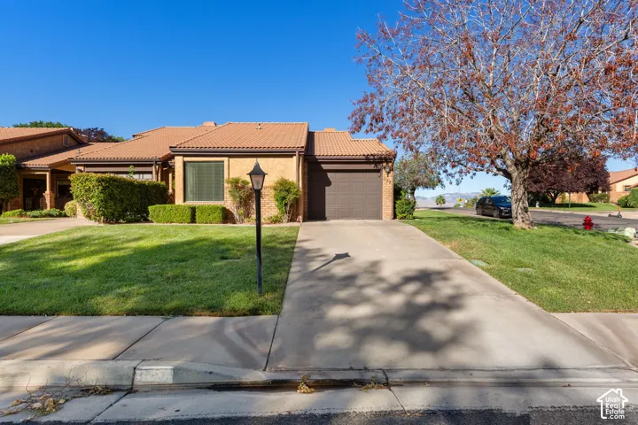 Brick exterior with a tiled roof, mature landscaping, and an attached garage with a paved driveway