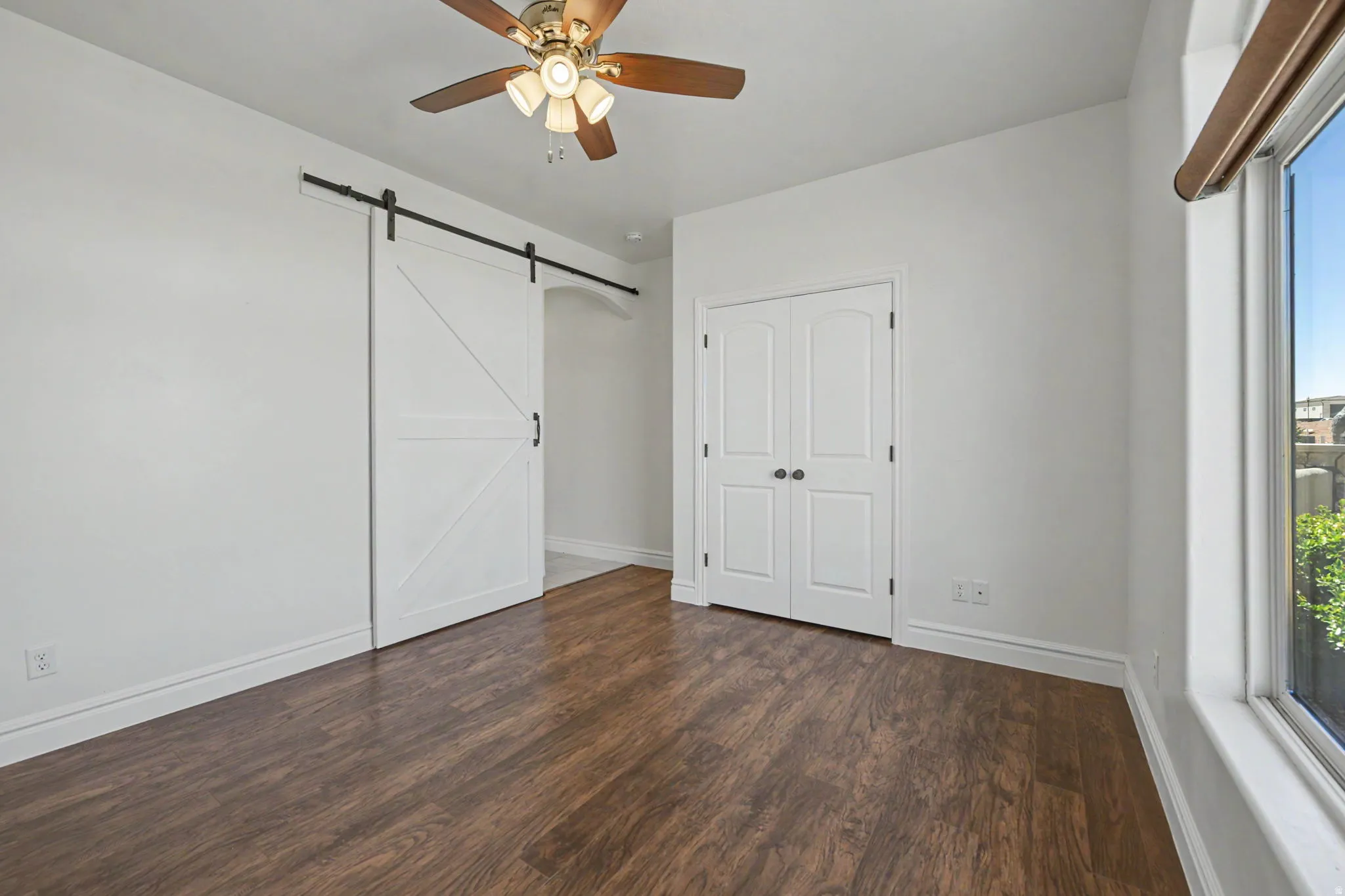 Wood-finish flooring, white walls, white double-door closet, white barn door, and a ceiling fan
