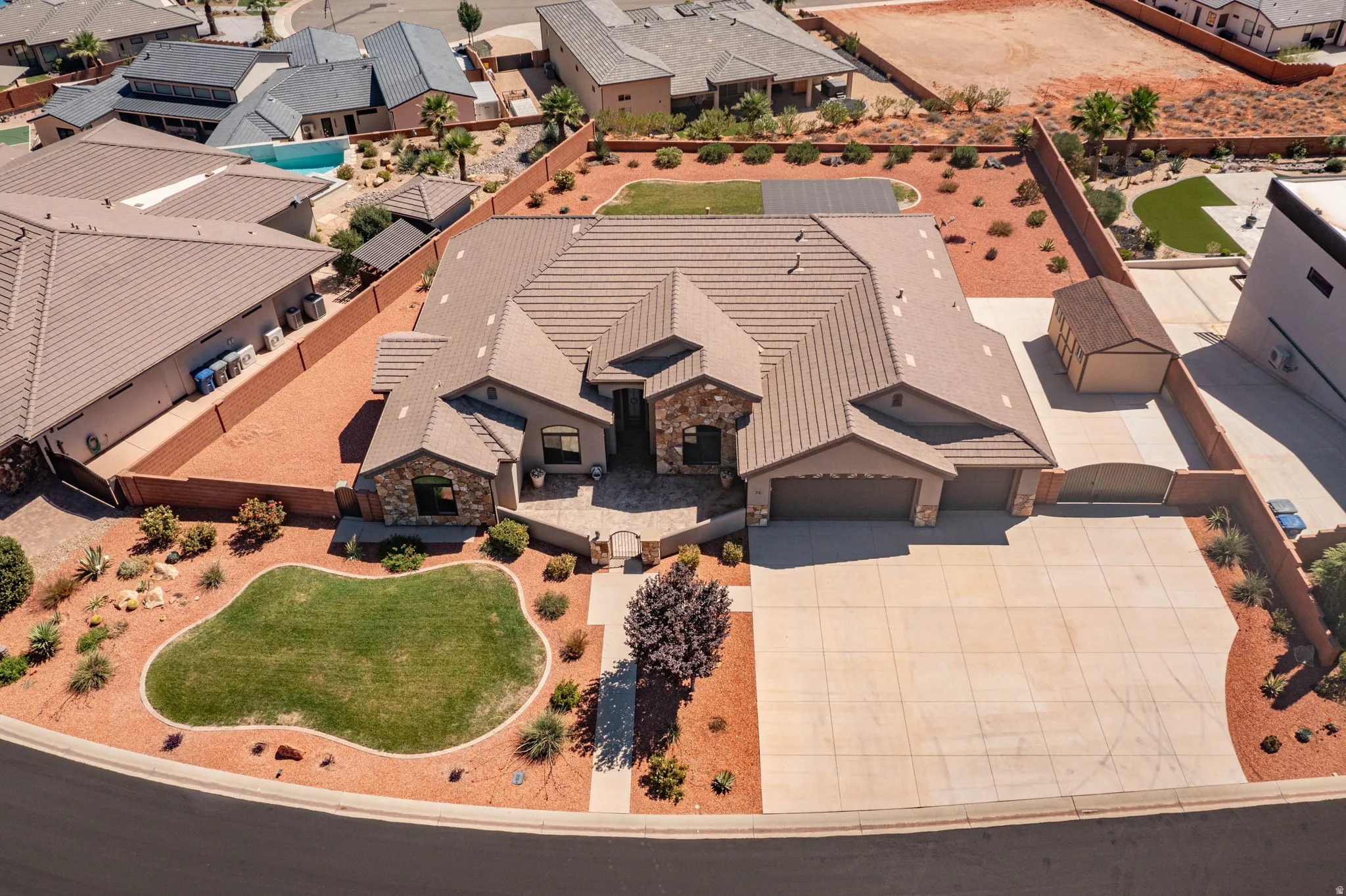 Expansive concrete driveway, attached two-car garage, stone and stucco exterior, tiled roof, and a detached shed