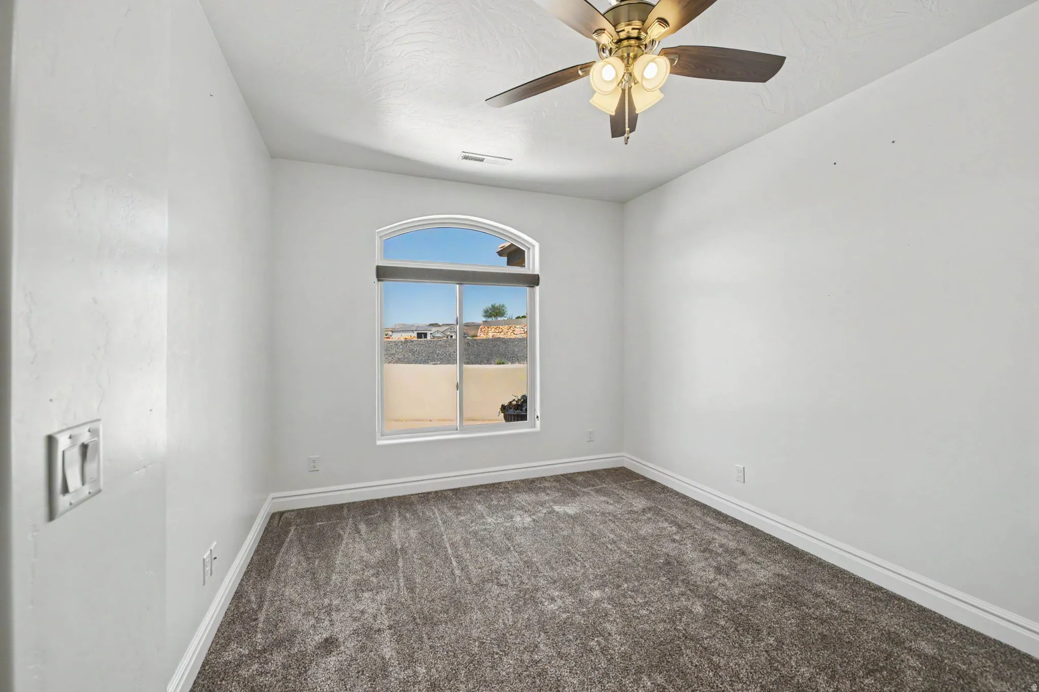 Arch-top window with blinds, textured ceiling, ceiling fan with integrated lighting, and carpeted flooring
