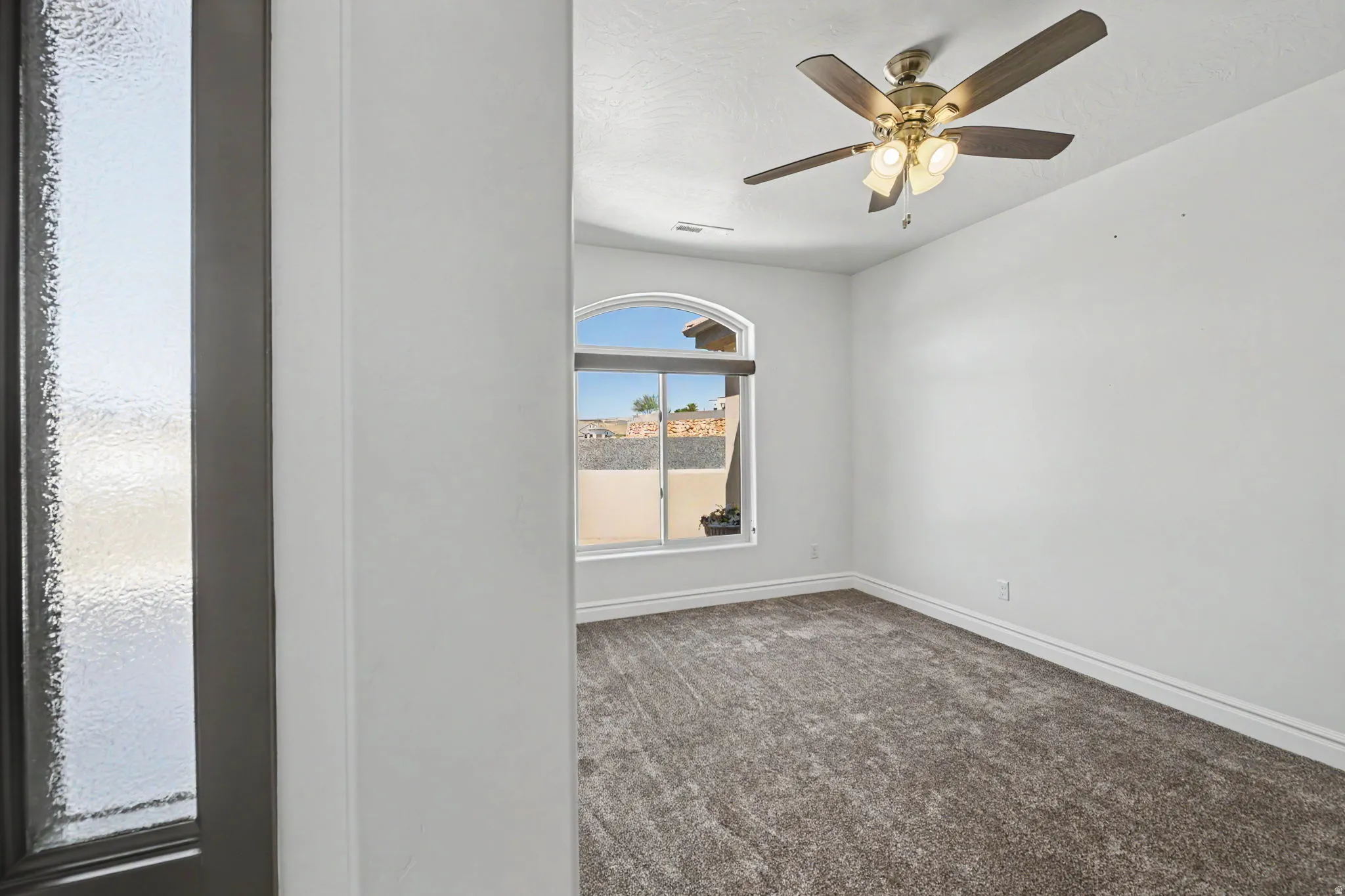 Arched window, ceiling fan, white walls, carpeted flooring, and white trim