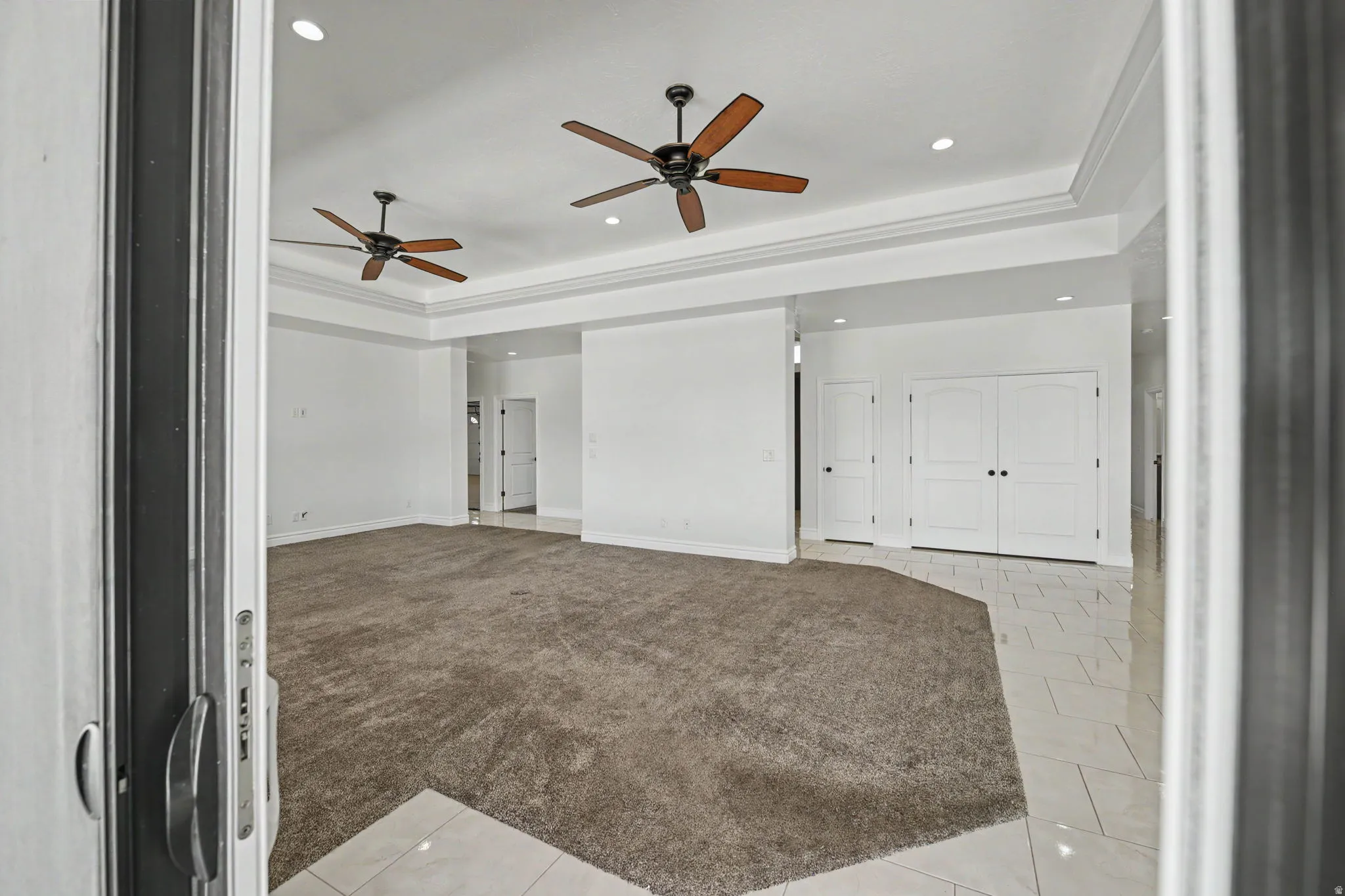 Spacious room featuring tray ceilings with recessed lighting, two ceiling fans, plush carpeting, and tile flooring