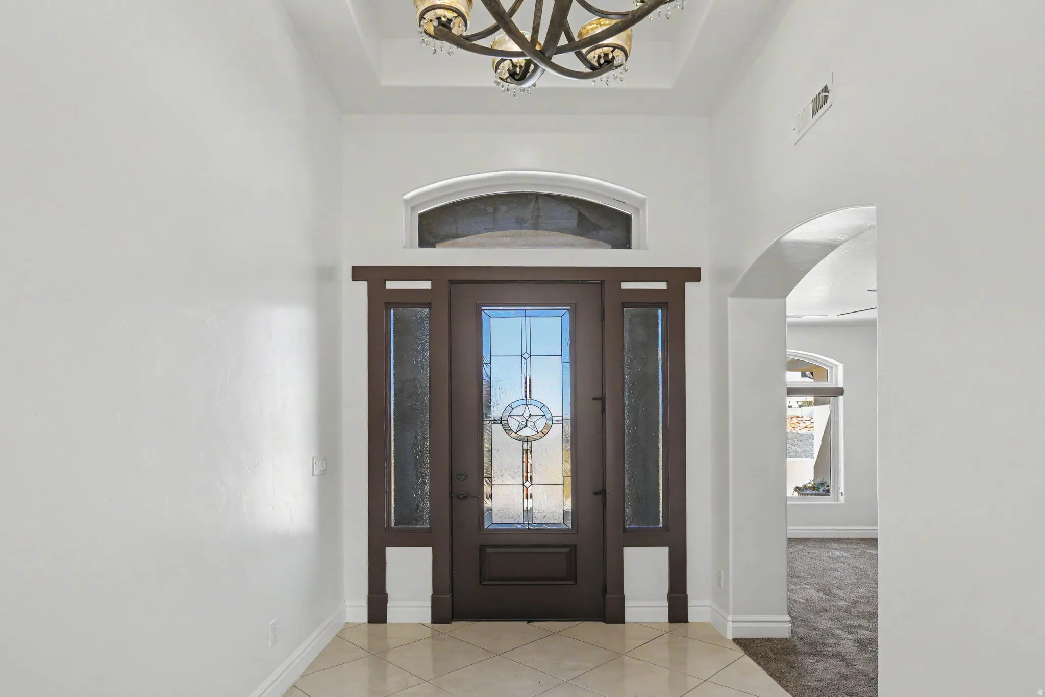 Entryway featuring a decorative transom window, leaded glass front door, side panel windows, and a coffered ceiling with an attached chandelier