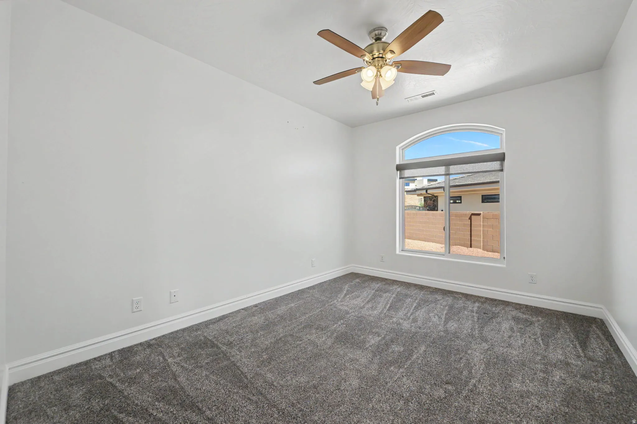 Neutral wall tones, gray carpeting, an arched window, and a ceiling fan with integrated lighting