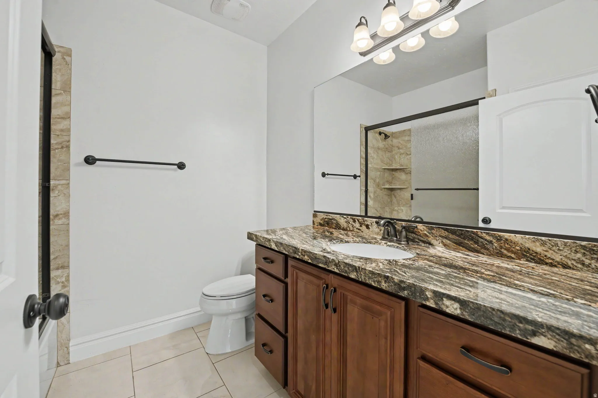 Vanity with a stone countertop and integrated sink, framed mirror, and wood-finish cabinetry with dark hardware
