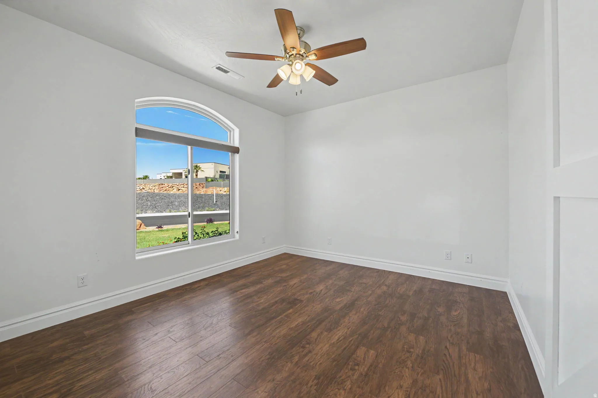 Arched window, wood-finish flooring, ceiling fan with integrated lighting, and white wall paneling