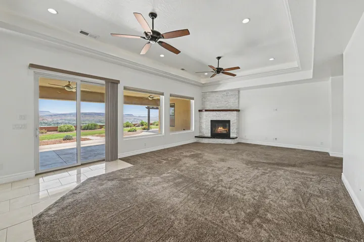 Tray ceiling with recessed lighting, ceiling fans, gas fireplace with stone surround, and direct patio access