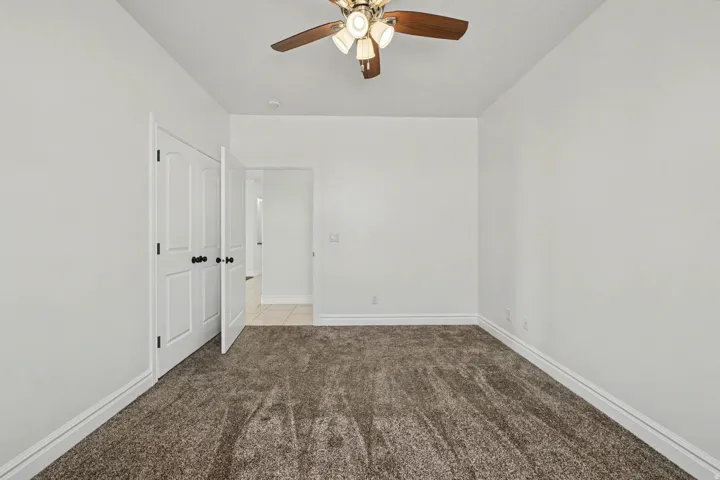 Neutral-toned carpet flooring, white walls, and a ceiling fan with light fixture