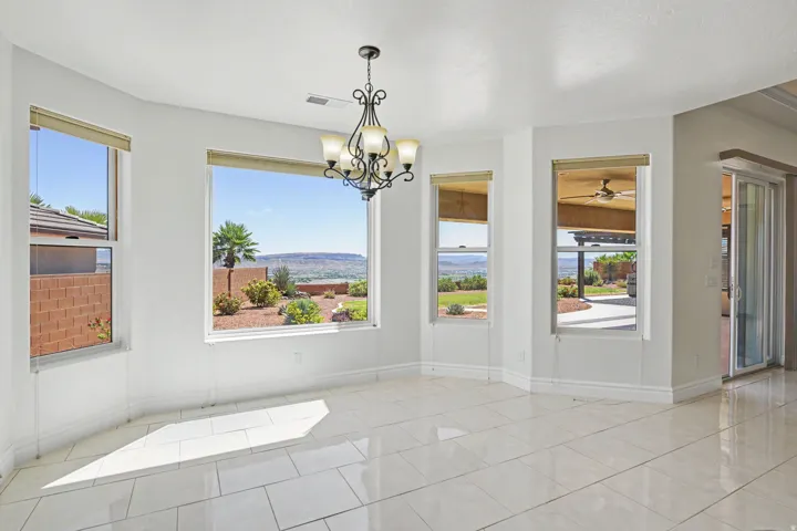 Bright, open great room showcasing polished tile flooring, abundant natural light from multiple expansive windows, and a decorative chandelier