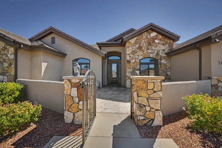 Stucco exterior with stone accents, arched entry door, tiled roofing, and a decorative metal gate