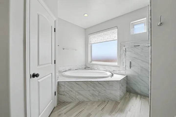Soaking tub with a tiled surround, a separate glass-enclosed shower, and wood-finish flooring