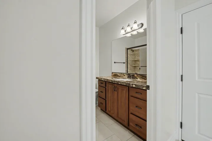 Bathroom featuring a wood-finish vanity with a stone-finish countertop, undermount sink, and a four-light vanity fixture