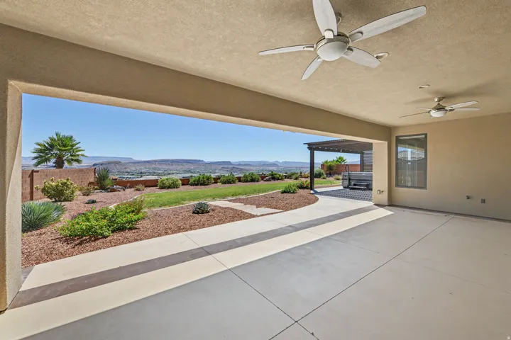 Expansive covered patio with dual ceiling fans, concrete flooring, and a desert landscape with distant mountains