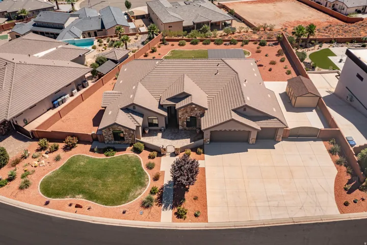 Expansive concrete driveway, attached two-car garage, stone and stucco exterior, tiled roof, and a detached shed