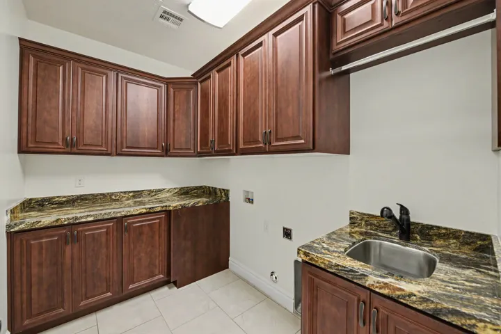 Cabinetry with a rich wood finish, stone countertops, a stainless steel sink, a matte black faucet, and tile flooring