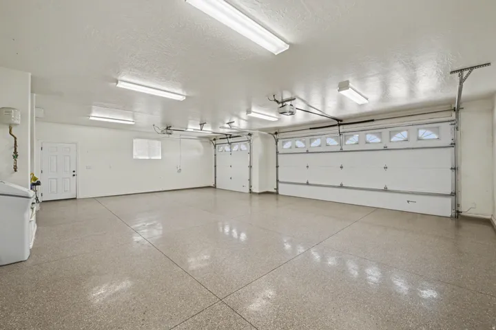 Attached three-car garage featuring segmented garage doors with upper window panels, a utility access door, and an epoxy-coated concrete floor