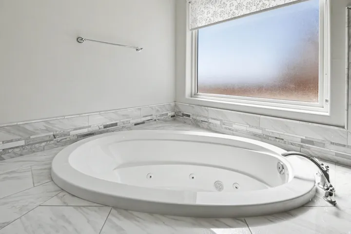 Built-in soaking tub with polished chrome fixtures, surrounded by large format tile flooring and a decorative tile accent wall