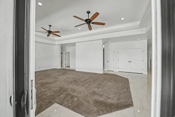 Spacious room featuring tray ceilings with recessed lighting, two ceiling fans, plush carpeting, and tile flooring