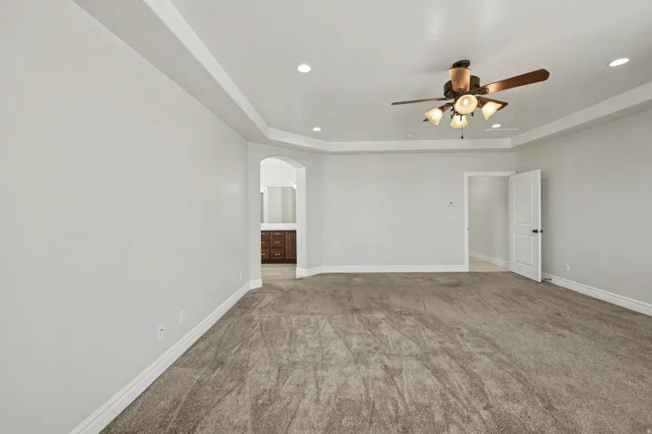 Tray ceiling with recessed lighting, ceiling fan light fixture, arched doorway, and neutral-toned carpet flooring