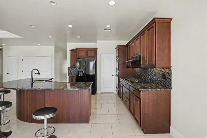 Kitchen featuring a dark wood-finish cabinetry, a large kitchen island with integrated sink, dark speckled countertops, and a mosaic tile backsplash