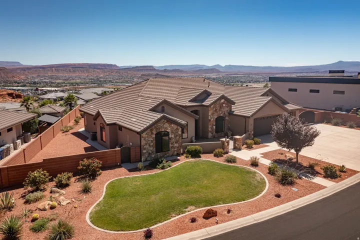 Stucco exterior with stone accents, a multi-car garage, front lawn, and desert-style landscaping