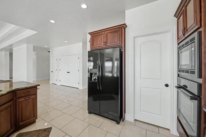 Kitchen featuring built-in stainless steel double ovens and microwave, wood-finish cabinetry, a black French door refrigerator, and tile flooring