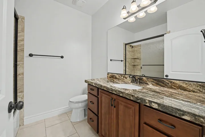 Vanity with a stone countertop and integrated sink, framed mirror, and wood-finish cabinetry with dark hardware