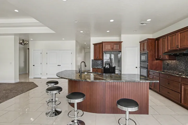 Spacious kitchen featuring an expansive island with a built-in sink, rich wood cabinetry, and a dark mosaic tile backsplash