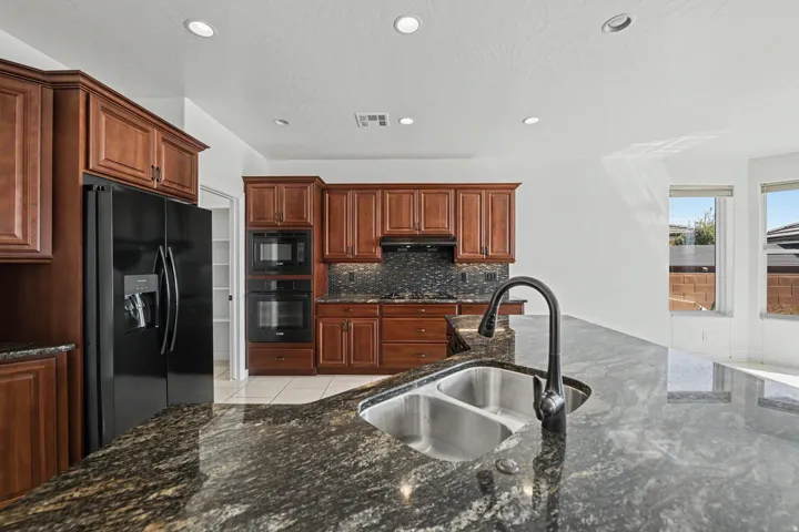 Kitchen featuring rich wood cabinetry, built-in stainless steel appliances, dark granite countertops, a double basin sink, and recessed lighting