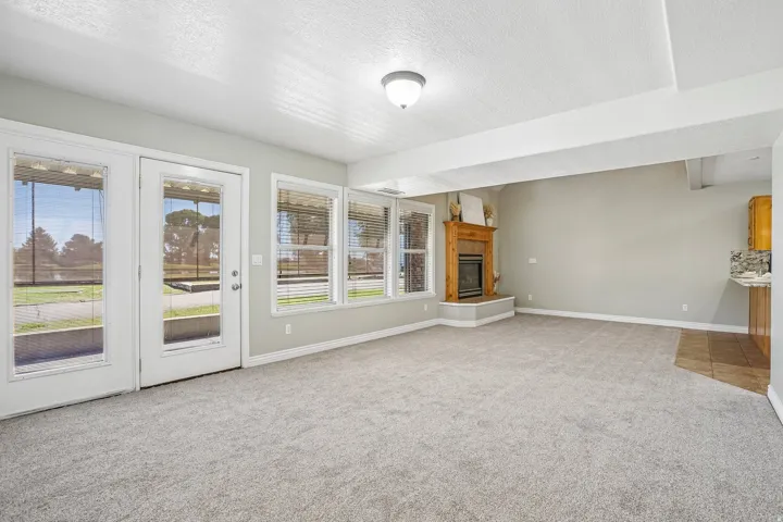 Spacious room featuring light gray carpeting, multiple windows with blinds, and a built-in fireplace with a wood mantle