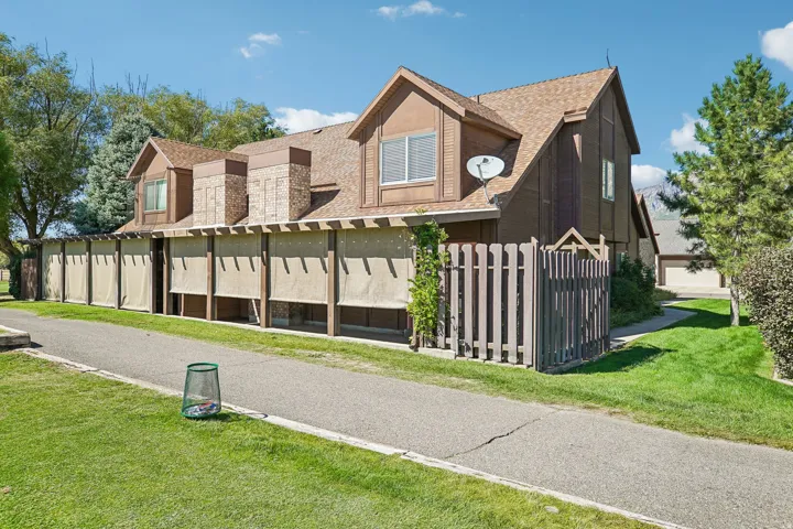 Brown-toned exterior with a shingled roof, dormer windows, and a privacy fence
