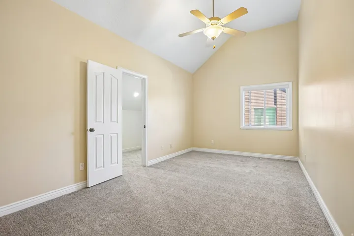 Vaulted ceiling, ceiling fan, gray carpet, white trim, and a window with blinds