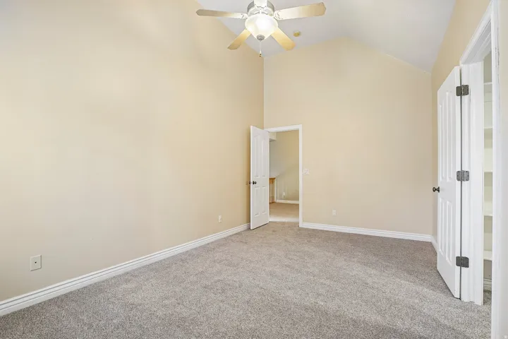 Vaulted ceiling with a ceiling fan, plush carpet flooring, and a built-in closet with shelving