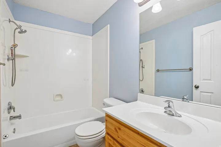 Full bathroom featuring a single vanity with wood-finish cabinetry, a wide mirror, a bathtub with a shower combination, and light blue wall paint