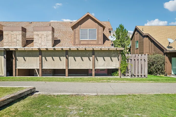 Brown exterior siding with a light brown shingle roof, featuring multiple dormer windows, brick chimneys, and an open pergola structure