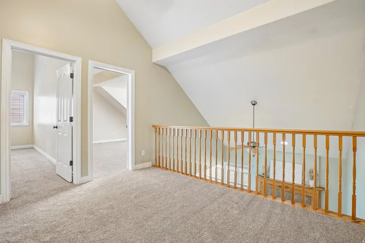 Carpeted loft area with vaulted ceilings, natural wood railing, and two room entrances