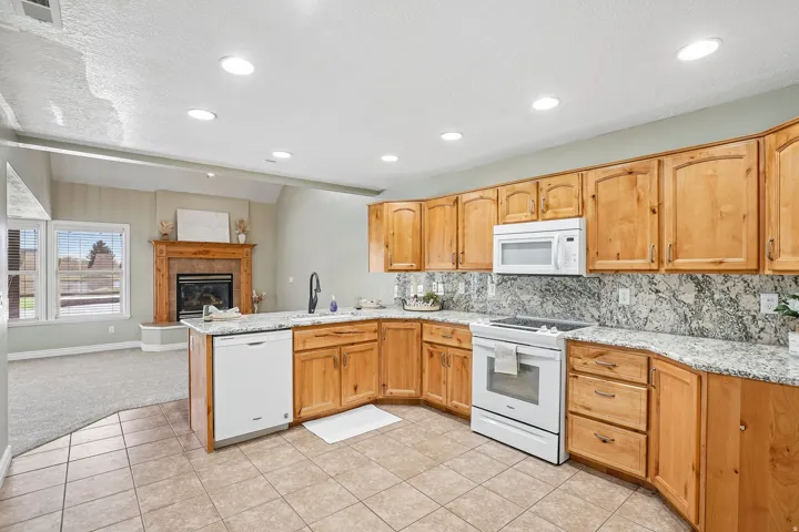 Kitchen featuring light wood cabinetry, stone countertops, a tile backsplash, and recessed lighting