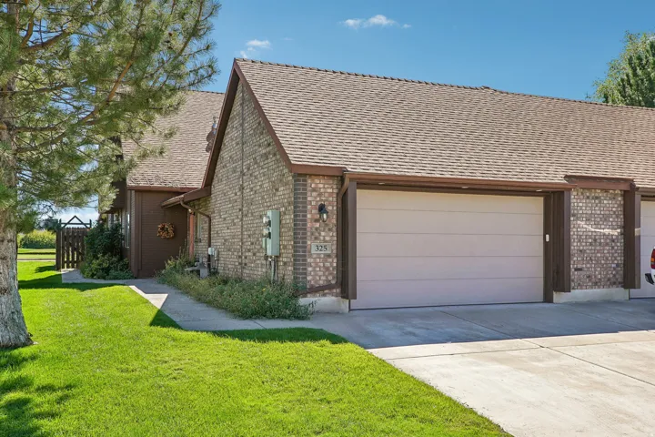 Brick exterior with a brown shingle roof, attached garage, and a concrete driveway