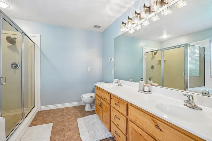Dual vanity with integrated sinks, wood-finish cabinetry, frameless glass shower enclosure, and tiled flooring