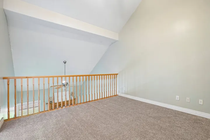 Loft space featuring sloped ceilings, light-toned carpeting, and a natural wood-finish railing