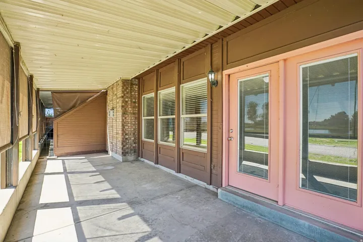 Covered patio featuring a concrete floor, brick column accent, multiple windows with blinds, and a double-door entry