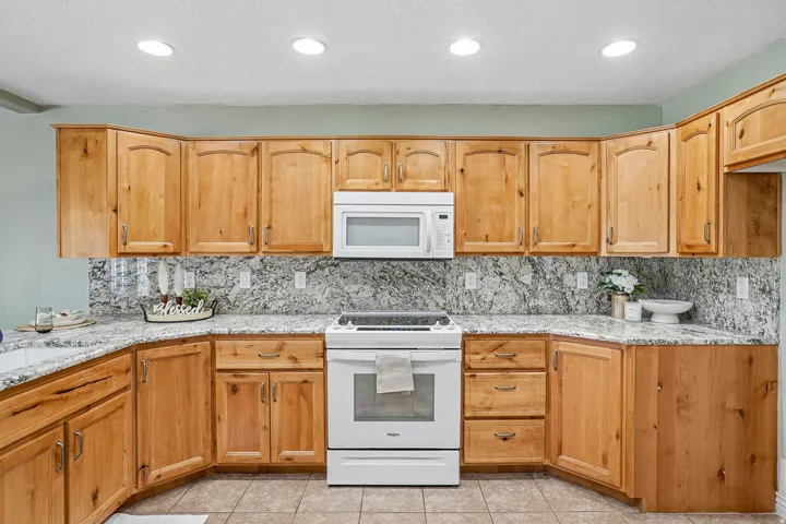 Wood-finish cabinetry with silver-tone hardware, white appliances, recessed lighting, and tile flooring