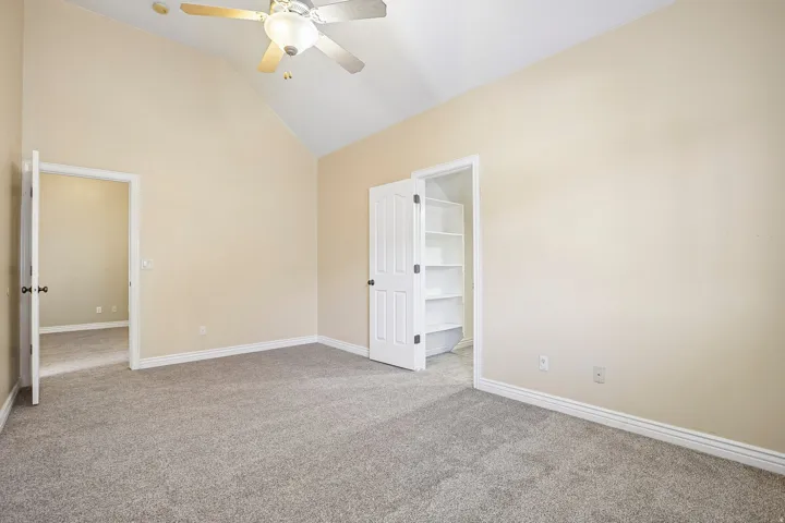 Vaulted ceiling with a ceiling fan, neutral carpet, and built-in shelving