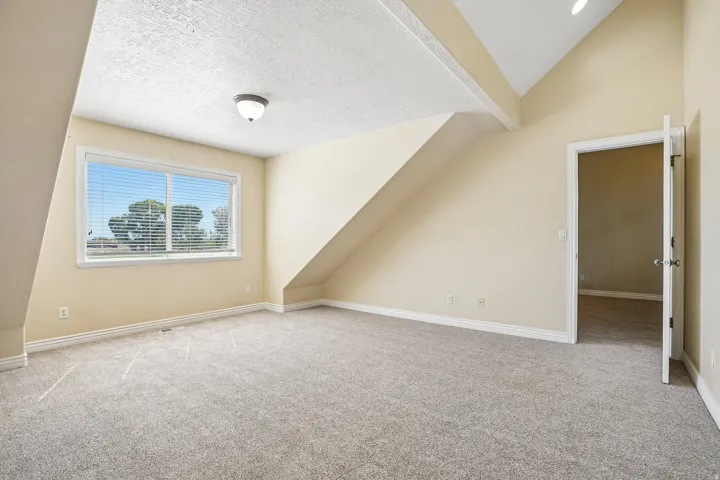 Vaulted ceiling with exposed beam, window with blinds, light-colored carpeting, and neutral wall paint